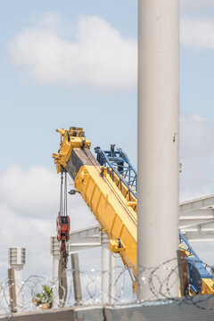 View of a yellow mobile crane boom at a construction site near Tirana International Airport with a white metal frame structure and barbed wire fence in Rinas, Albania.