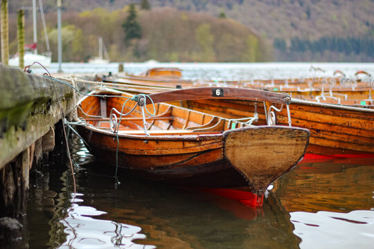 Traditional wooden rowing boats tied to wooden jetty on Windermere at Bowness-on-Windermere Lake District Cumbria England
