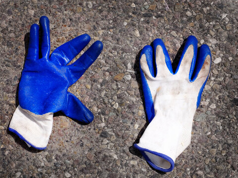 Old Abandoned Rubber Work Gloves Blue and  White Laying on Asphalt Road Roadway