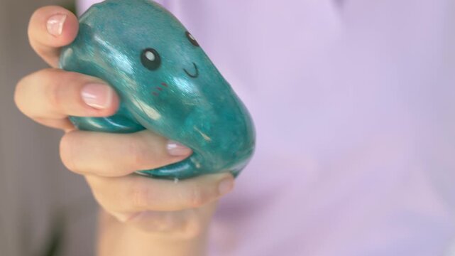 Fingers press squishy character toy into shape closeup revealing round eyes and curved mouth carefully. Playful tactile squeeze motion demonstrates soft stress relief toy for calm moments 