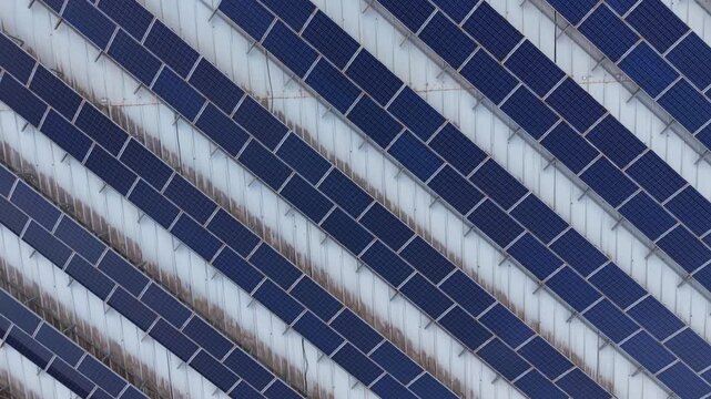 Overhead view of a large solar farm featuring rows of blue photovoltaic panels arranged in a repeating diagonal pattern, generating renewable clean energy
