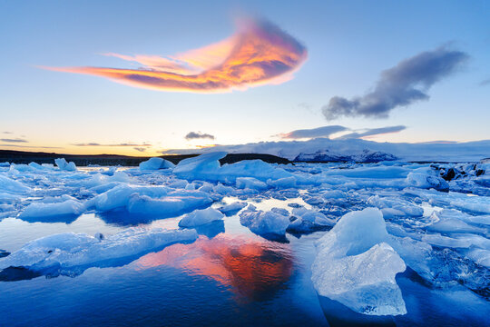 View of icebergs floating in a glacial lagoon under a colorful sunset sky with vibrant cloud reflections on the water, Iceland.