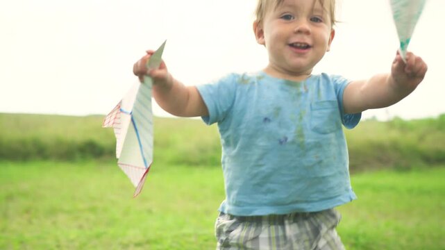 Toddler smiling directly at camera while holding paper airplane