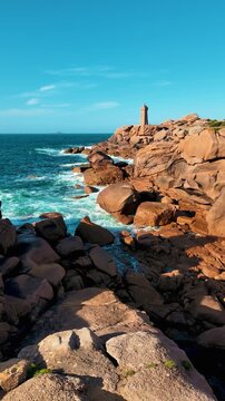 Plan fixe sur la c&ocirc;te de granit rose &agrave; Perros-Guirec, en Bretagne, avec le phare de Mean Ruz dominant les imposants rochers de granit sculpt&eacute;s par la mer. 