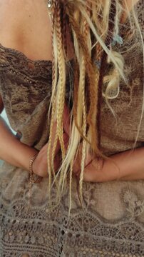 Woman seen from behind with blonde dreadlocks and braided accents, wearing a bohemian dress, standing outdoors in a calm, reflective moment of mindful tranquility and natural freedom