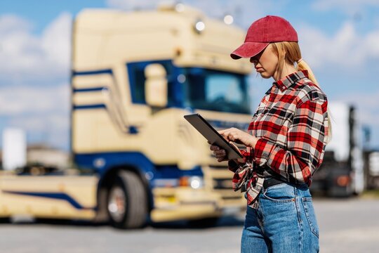 Woman truck driver using a tablet computer in front of a semi-trailer truck