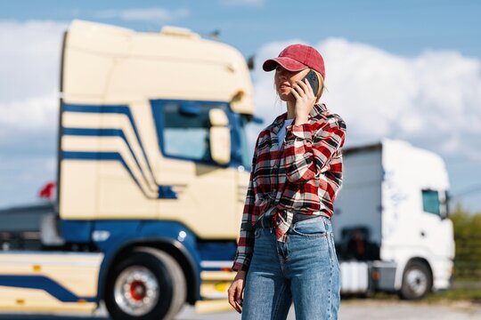 Woman trucker in casual attire using a mobile phone near semi-trucks