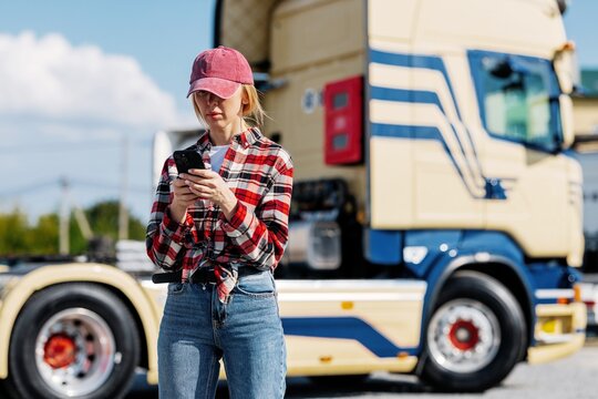 Woman truck driver using smartphone while standing next to semi-truck