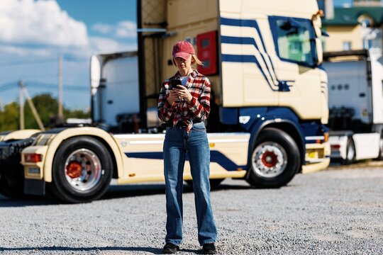 Woman trucker checking her phone while standing next to a semi-truck
