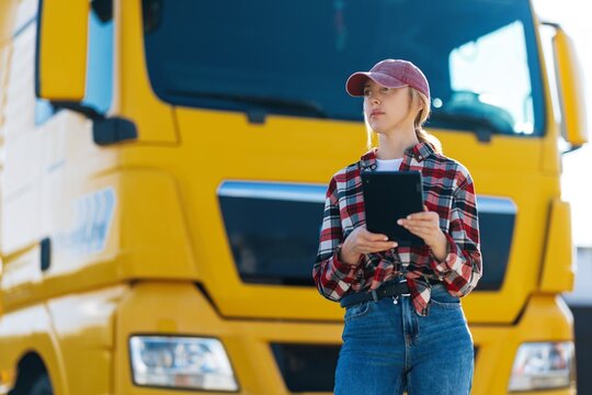 Female truck driver with tablet in front of a yellow semi-truck