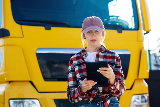Woman truck driver holding a tablet in front of a large yellow semi-truck