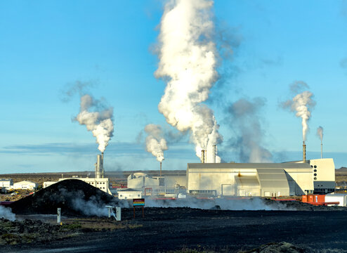 View of the Svartsengi Geothermal Power Plant with steam rising from industrial chimneys against a clear blue sky in Grindavik, Grindavikurbaer, Iceland.