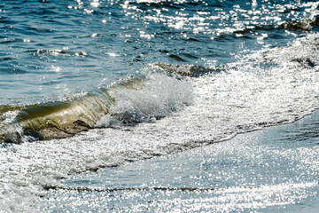 Clear blue ocean water sparkles under the bright afternoon sun while small waves gently roll toward the sandy shoreline creating a refreshing scene of peaceful nature and calm movement by the sea © Lilly