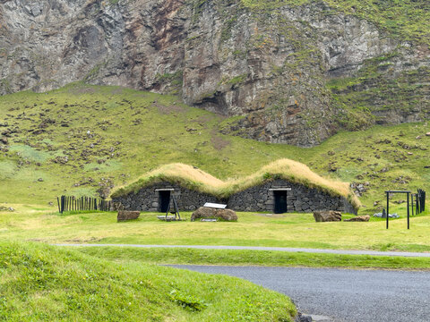 View of traditional turf houses with grass roofs nestled at the base of a steep rocky mountain in Eyjafjallajokull, Rangarthing eystra, Iceland.
