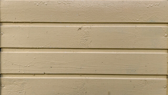 Beige yellow painted wood siding planks creating a rustic textured background with peeling paint and visible grain, representing a weathered surface or wall paneling