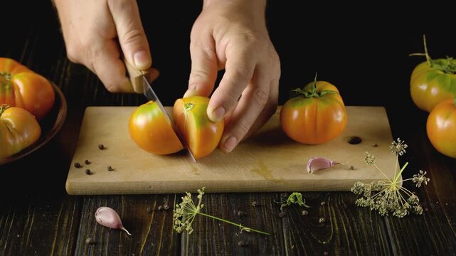 Hands of a person slicing ripe tomatoes on a wooden cutting board, with additional tomatoes and shallots arranged around, creating a vibrant kitchen scene filled with fresh ingredients