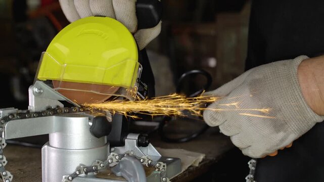 Worker sharpens a chainsaw chain using an electric sharpener with a yellow cover, sparks flying as the tool engages, showcasing the precision and care in a workshop environment
