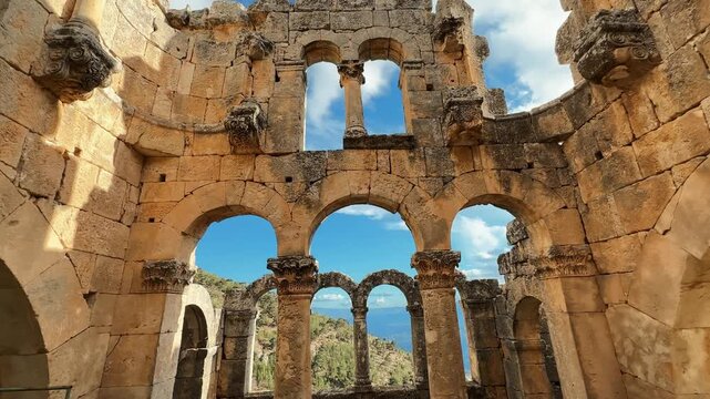 Moving through the ancient church at Alahan Monastery in Mut, Mersin, T&uuml;rkiye, then tilting upward to reveal stone arches and historic architecture.