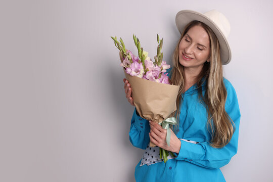 Woman with beautiful gladiolus flowers near white wall indoors, space for text