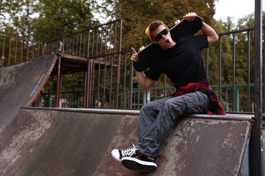 Stylish man with skateboard on ramp in skate park. Space for text