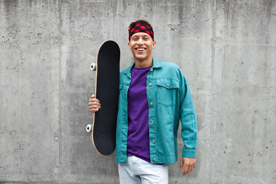Happy man with skateboard near grey wall outdoors