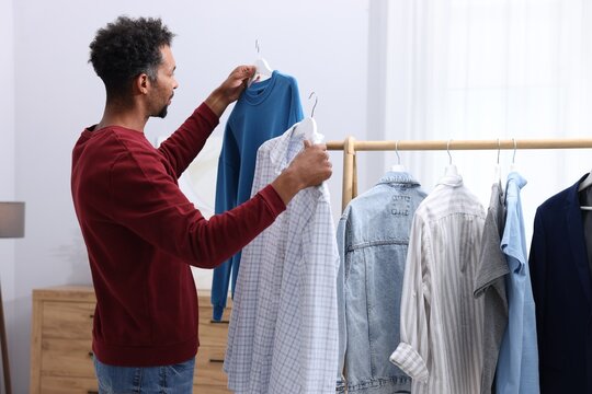 Man choosing between shirt and sweatshirt indoors