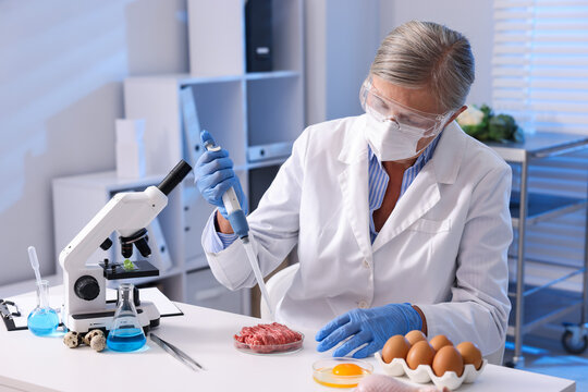 Quality control. Scientist in protective goggles, mask and gloves working with raw minced meat at white table in laboratory