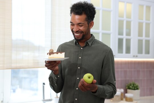 Man choosing between apple and dessert in kitchen