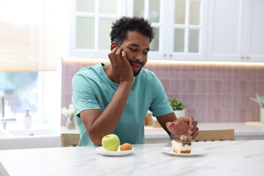 Man choosing between fruits and dessert at white marble table in kitchen
