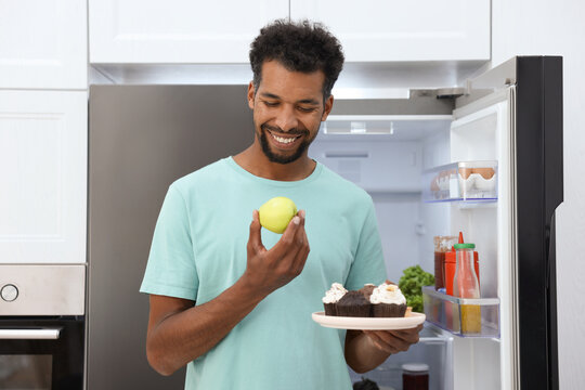 Man choosing between apple and desserts in kitchen