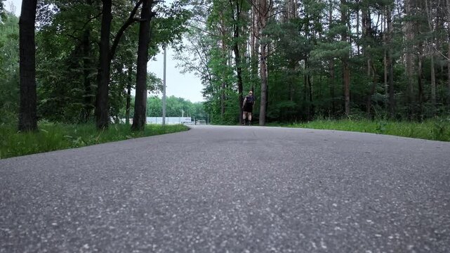 A roller skater glides along a path in the forest. Tall trees surround the area. The skater enjoys the open space while moving forward on the smooth ground.