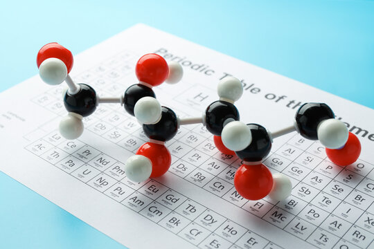 Chemical model of glucose molecule and periodic table on light blue background, closeup