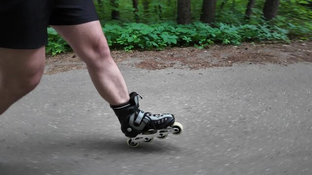 In a forest park, a skater moves smoothly on rollerblades. The strong legs help with balance and speed. The path is clear and lined with trees. Sunlight filters through the leaves.