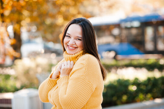 Smiling beautiful woman 30-35 year old wearing yellow knitted sweater over autumn leaves close up. Fall season. Looking at camera.