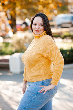 Smiling beautiful woman 30-35 year old wearing yellow knitted sweater over autumn leaves close up. Fall season.