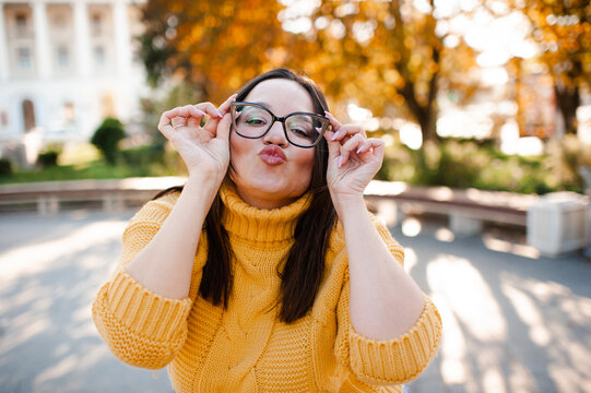 Smiling beautiful woman 30-35 year old wearing yellow knitted sweater and eye glasses over autumn leaves close up. Fall season. Looking at camera.