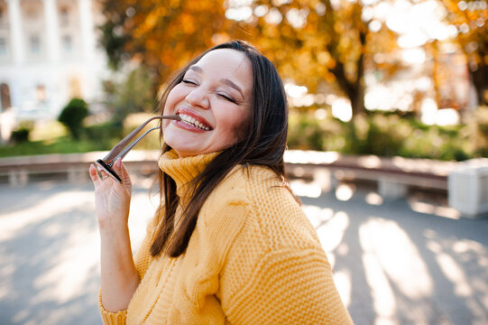 Smiling beautiful woman 30-35 year old wearing yellow knitted sweater and eye glasses over autumn leaves close up. Fall season.