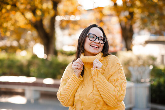 Smiling beautiful woman 30-35 year old wearing yellow knitted sweater and eye glasses over autumn leaves close up. Fall season.