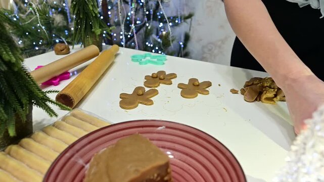 Beautiful hands carefully place gingerbread cookies on a table filled with decorations. The atmosphere is festive with a Christmas tree and garland around the scene.