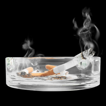 Smoldering cigarettes in ashtray against black background, closeup