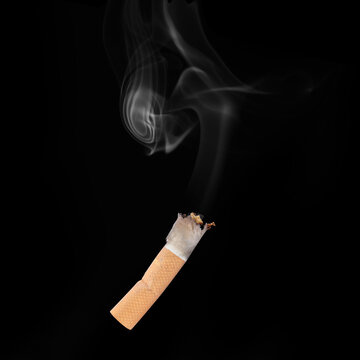Smoldering cigarette butt with rising smoke against black background