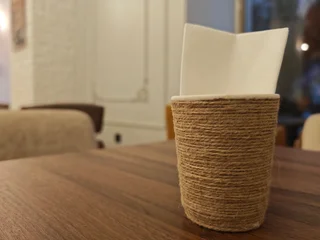 Fotobehang Horeca Rustic Jute Tissue Holder with White Napkins on Wooden Cafe Table  © JoyfulImages