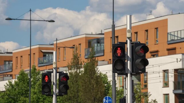 Timelapse of pedestrian and bicycle traffic lights changing from red to green at an urban intersection, with modern residential buildings and contemporary city architecture in the background