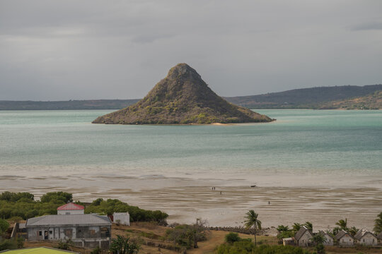 View of the conical Sugar Loaf Mountain rising from the turquoise waters of the bay with sandy tidal flats and coastal houses in the foreground in Antsiranana, Diana, Madagascar.