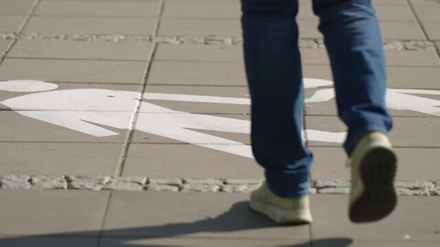 Close up of pedestrian walking away from camera over painted pedestrian path marking, feet in sneakers moving along designated urban walkway on sunny summer day