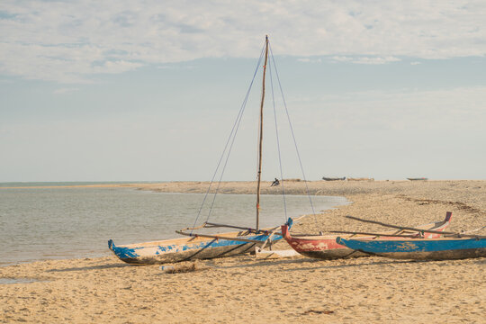 View of traditional wooden outrigger boats resting on the sandy shore under a clear sky in Morondava, Menabe, Madagascar.
