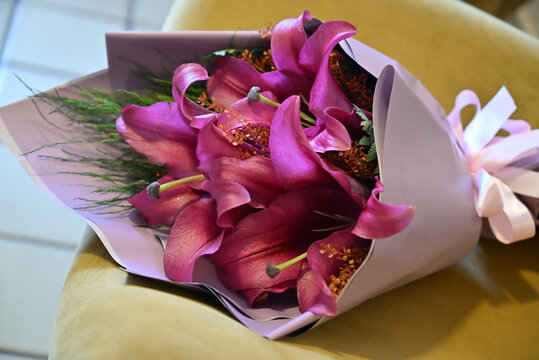 pink lily flower bouquet wrapped in light purple paper tied with satin ribbon, vibrant pink lilies floral arrangement resting on wooden table, elegant gift bouquet close up
