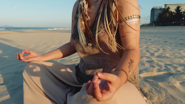 Woman with dreadlocks and temporary tattoos meditating in a lotus position on a peaceful beach, embracing a spiritual journey and mental well being at sunset, finding harmony and inner balance