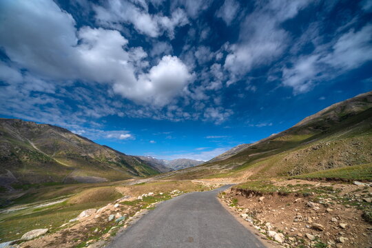 View of a paved road winding through the vast grassy plateau and rolling mountains of Deosai National Park in Astore, Gilgit Baltistan, Pakistan.