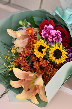 colorful flower bouquet wrapped in light green paper, vibrant floral arrangement with sunflower, peach lily, purple carnation and red chrysanthemums, gift bouquet close up